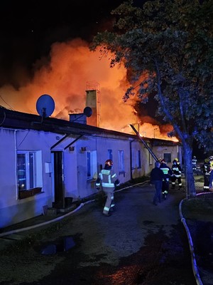 Strażacy przy budynku, nad którym widać łunę ognia.