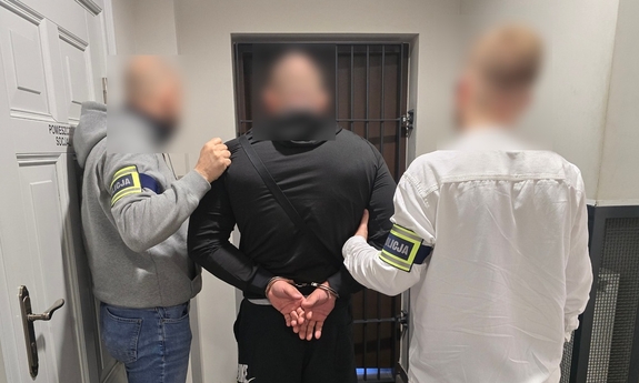 Dwaj funkcjonariusze trzymają zatrzymanego w kajdankach.