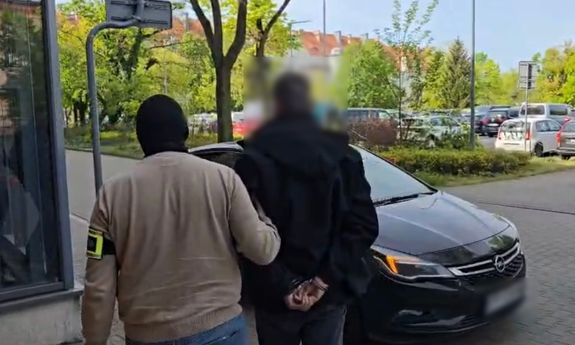 Ubrany po cywilnemu policjant prowadzi zatrzymanego do samochodu