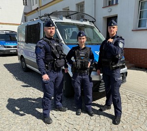 Trójka policjantów stoi przy radiowozie.