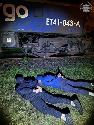 zatrzymani mężczyźni leżący na ziemi przy wagonie kolejowym