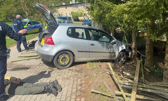 Samochód sprawców włamania. Jeden z zatrzymanych leży w kajdankach na ziemi. Obok policjanci.