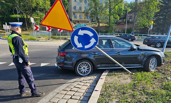 Policjant na miejscu wypadku, przy samochodzie.