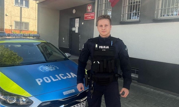 Policjant stoi przy radiowozie.