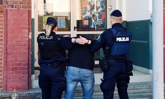 Policjant i policjantka wprowadzają do budynku komisariatu zatrzymanego mężczyznę.
