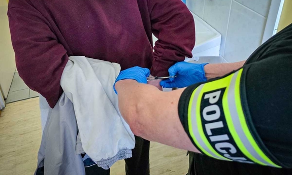 Zatrzymany zakuty w kajdanki prowadzony przez policjantów.