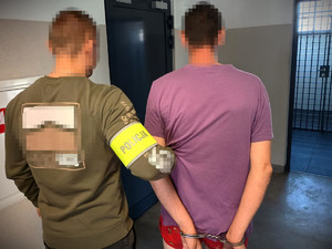 Policjant trzyma zatrzymanego mężczyznę zakutego w kajdanki.