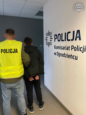 Nieumundurowany policjant w kamizelce odblaskowej z napisem Policja oraz zatrzymany mężczyzna.