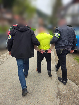 Na zdjęciu dwóch policjantów prowadzi zatrzymanego mężczyznę.