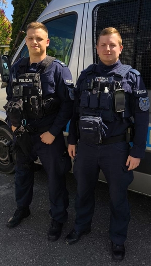 Dwaj policjanci, którzy uratowali życie mężczyźnie na lotnisku stoją przy radiowozie.