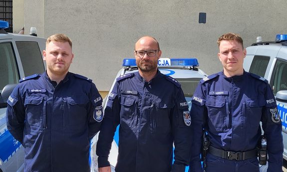 Na zdjęciu trzech umundurowanych policjantów. Za nimi trzy radiowozy.