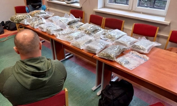 Zabezpieczona marihuana w foliowych woreczkach na stole.  Obok siedzi na krześle mężczyzna.