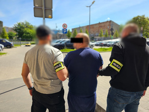 Dwaj funkcjonariusze prowadzą zatrzymanego.