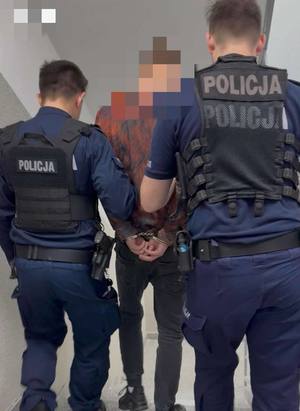 Dwaj funkcjonariusze prowadza zatrzymanego.