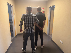 Ubrany po cywilnemu policjant prowadzi zatrzymanego.