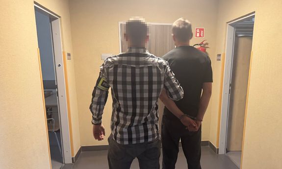Nieumundurowany policjant prowadzi zatrzymanego - widok z tyłu.