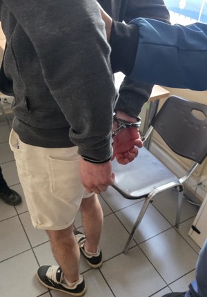 Zatrzymany mężczyzna w kajdankach na rękach trzymanych z tyłu.