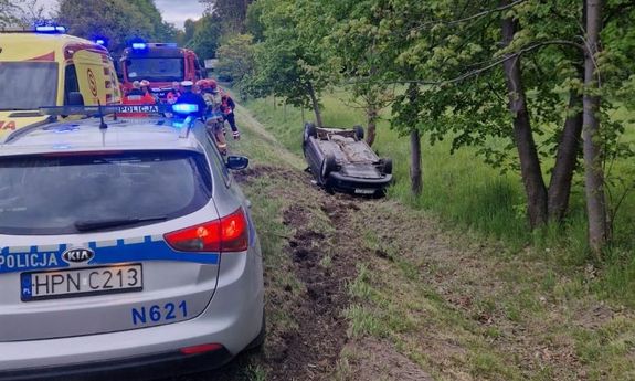 Samochód w rowie, a na poboczu widoczny radiowóz policyjny, karetka i wóz straży pożarnej.