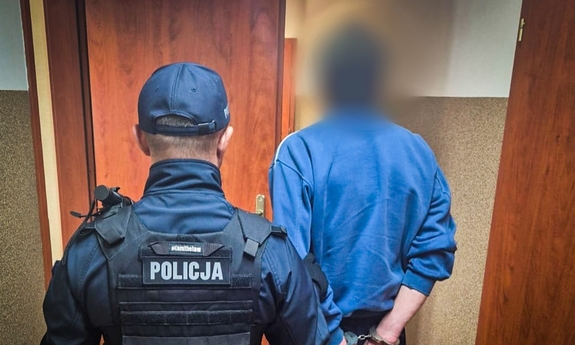 Umundurowany policjant prowadzi zatrzymanego mężczyznę.