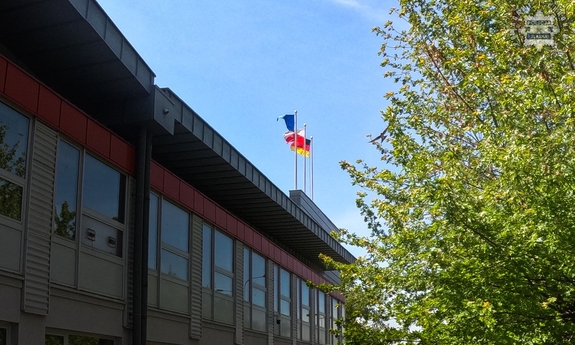Na dachu budynku powiewają trzy flagi: Polski, Niemiec i Unii Europejskiej.