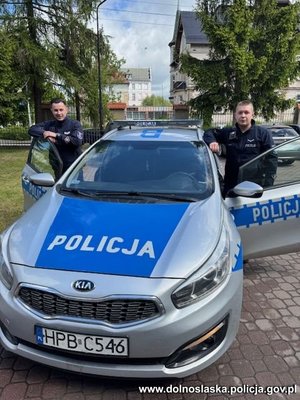 Dwaj funkcjonariusze stoją przy radiowozie.