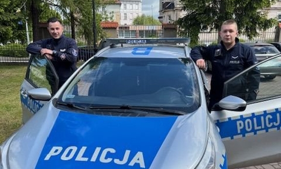 Dwaj funkcjonariusze stoją przy radiowozie.