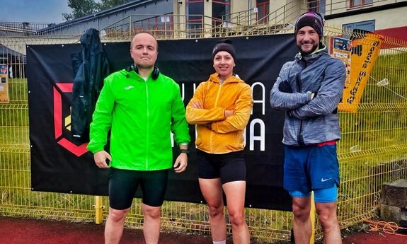 Dwóch mężczyzn i jedna kobieta na bieżni w strojach sportowych.
