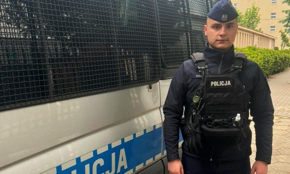 policjant stoi obok radiowozu.