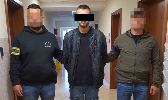 Dwaj funkcjonariusze z zatrzymanym mężczyzna w kajdankach.