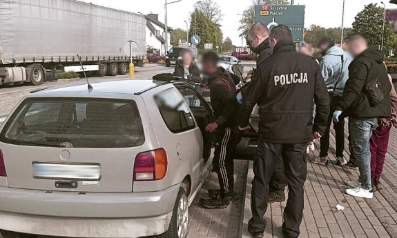 Policjanci i zatrzymane osoby przy samochodzie osobowym.