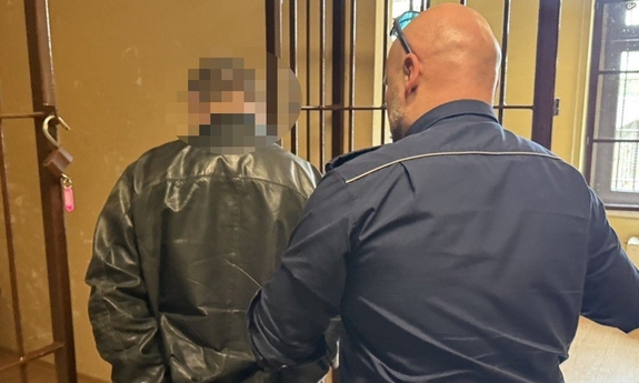 Funkcjonariusz prowadzi zatrzymanego mężczyznę.