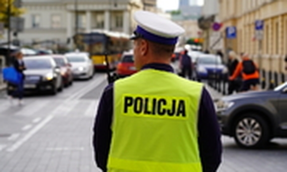 Odwrócony tyłem policjant stoi na ulicy.