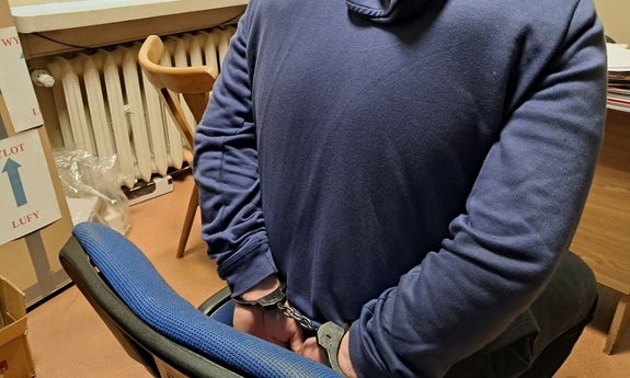 Zatrzymany siedzi na krześle z kajdankami założonymi na ręce trzymane z tyłu.