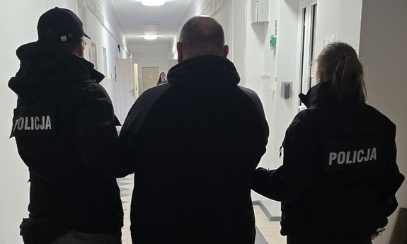 Dwaj funkcjonariusze prowadzą zatrzymanego.