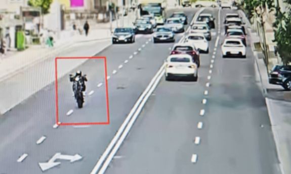 kadr z monitoringu. motocyklista jedzie na jednym kole. w tle widać samochody.