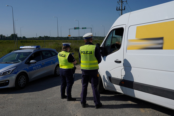 Dwaj policjanci stoją przed kontrolowanym autem.