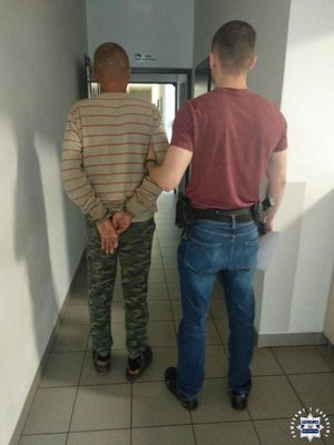 zatrzymany mężczyzna w kajdankach prowadzony przez funkcjonariusza policji ubranego po cywilnemu