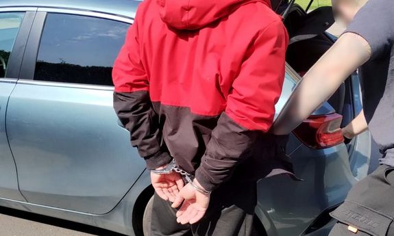 Zatrzymany obywatel Mołdawii w kajdankach na rękach i policjant przed autem.