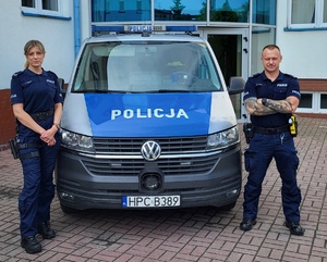 Dwoje umundurowanych policjantów stoi przy policyjnym furgonie.