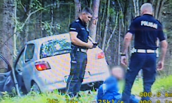 Policjanci z zatrzymanym mężczyzną przy samochodzie.