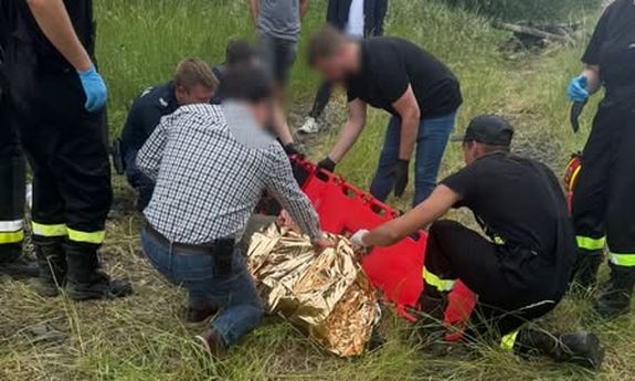 Mężczyźni przy leżącym na ziemi zaginionym, odnalezionym po poszukiwaniach, który owinięty jest w koc termiczny.