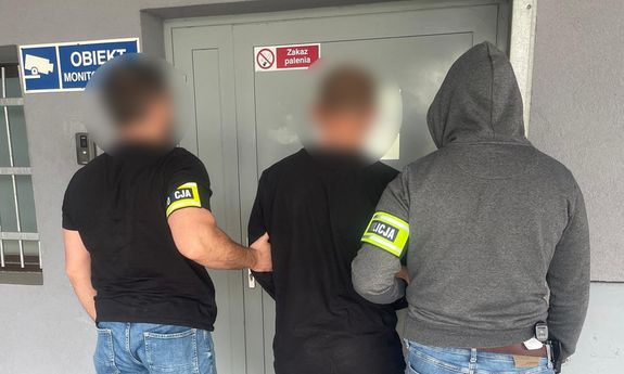 Dwaj nieumundurowani policjanci prowadzą zatrzymanego. Widok z tyłu.