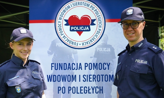 Policjant i policjantka na tle banneru z napisem: Fundacja Pomocy Wdowom i Sierotom po Poległych policjantach.