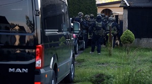 Grupa policyjnych kontrterrorystów na akcji przed bramą posesji. Na pierwszym planie widoczny fragment czarnego samochodu.