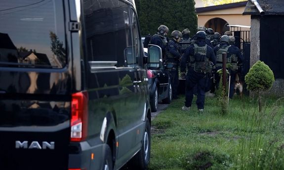 Grupa policyjnych kontrterrorystów na akcji przed bramą posesji. Na pierwszym planie widoczny fragment czarnego samochodu.