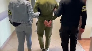 Zatrzymany prowadzony przez nieumundurowanych policjantów. Widok z tyłu.