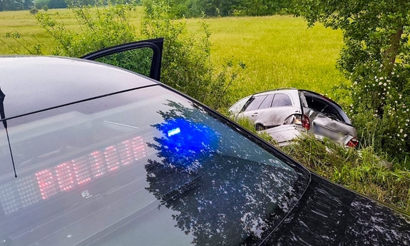 Na pierwszym planie fragment radiowozu policyjnego, w głębi samochód w rowie.