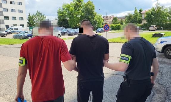 Dwaj funkcjonariusze prowadzą zakutego w kajdanki mężczyznę.