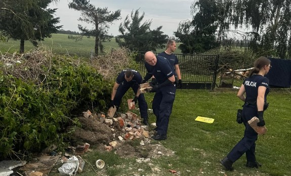 Policjanci sprzątają rozrzucone na posesji cegły po przejściu nawałnicy.
