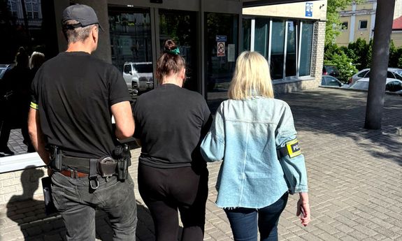 Dwoje nieumundurowanych policjantów prowadzi zatrzymaną kobietę.